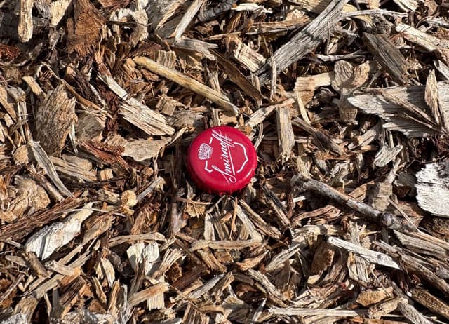 a red crinkle bottle cap laying in woodchips